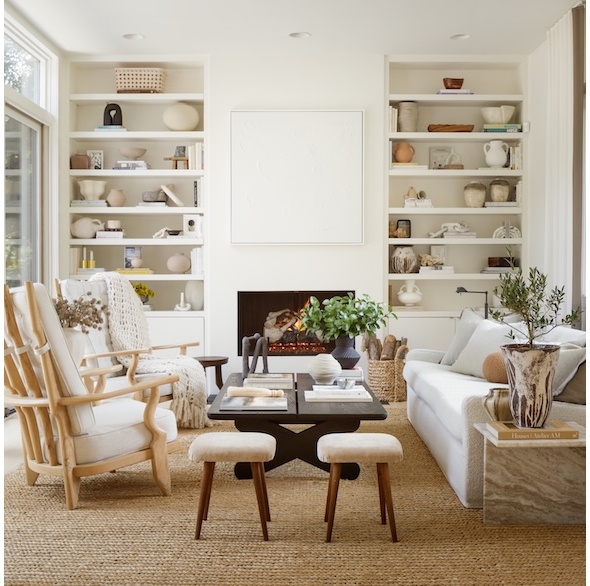 A styled white-on-white and wood-toned living room with built-in bookshelves flanking a fireplace. | BRG