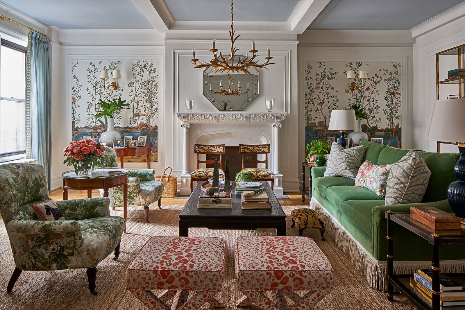A Grandmillennial living room decorated with an elegant green velvet sofa, two floral upholstered chairs, a classic fireplace adorned with a heptagon mirror, and four accent chairs with wild upholstery