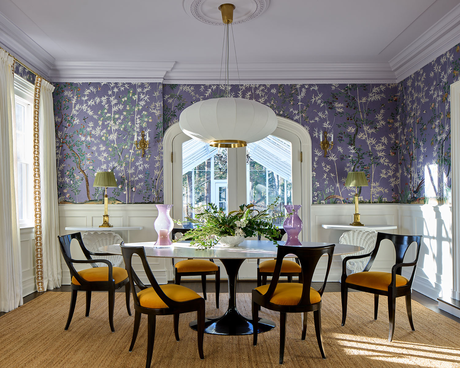 Elegant dining room adorned in rich violet hues, with floral wallpaper and vases. A contemporary round table with black and orange chairs juxtaposes the otherwise traditional decor.