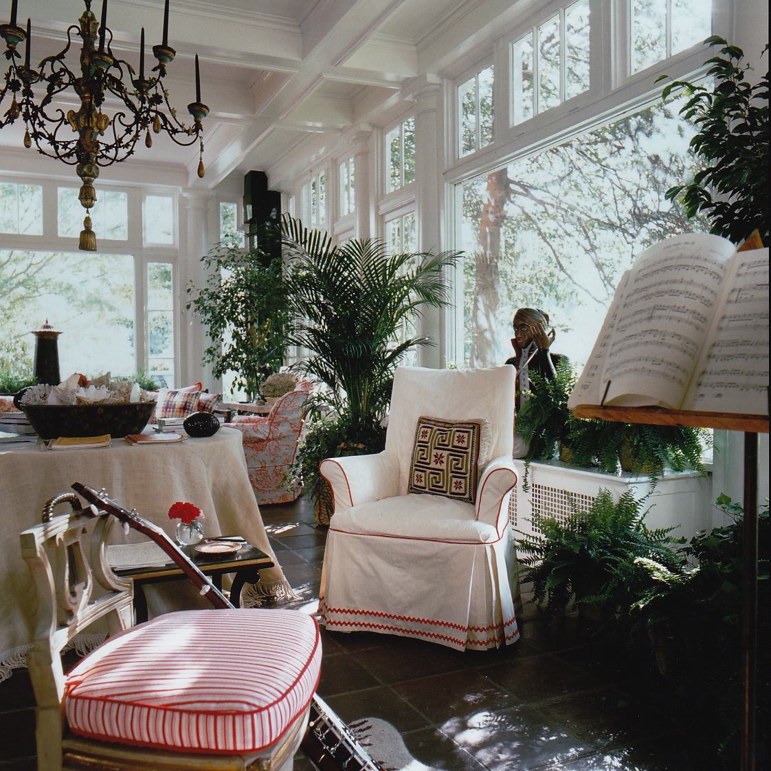 A beautifully appointed sunroom is filled with natural light from numerous windows. The space is enhanced with plants, furniture, and decorative accents.