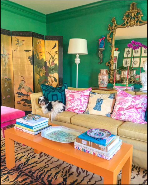 A vibrant green living room filled with other colorful tones such as pink pillows, orange coffee table, and yellow/gold accents in the gilt mirror and Asian folding screen, all upon a large animal print area rug.