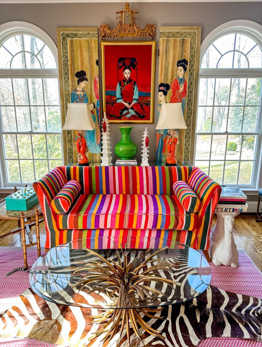Contrasting patterns in a variety of bold colors make this room sing with a zebra pattern rug under a multi-colored striped sofa with Asian portrait of a  noblewomen on the wall.