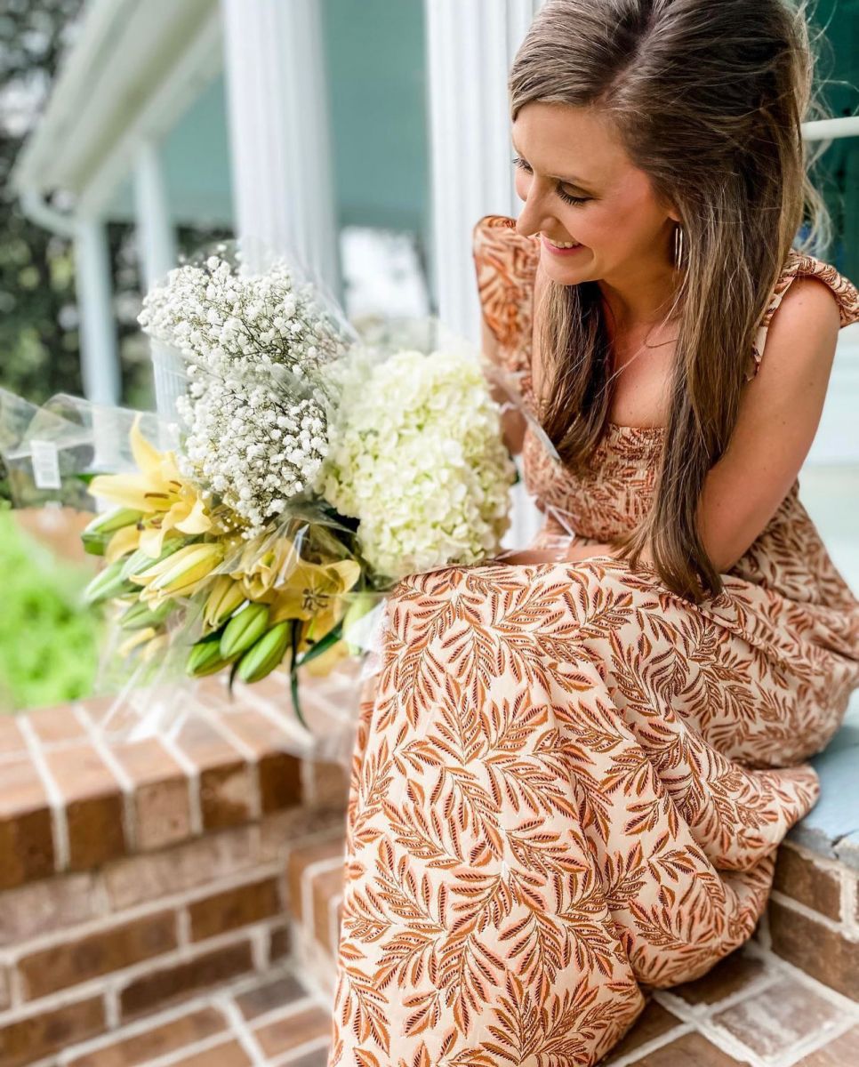 Interior designer, Jennifer Evans, sits on a porch step holding a bouquet of flowers