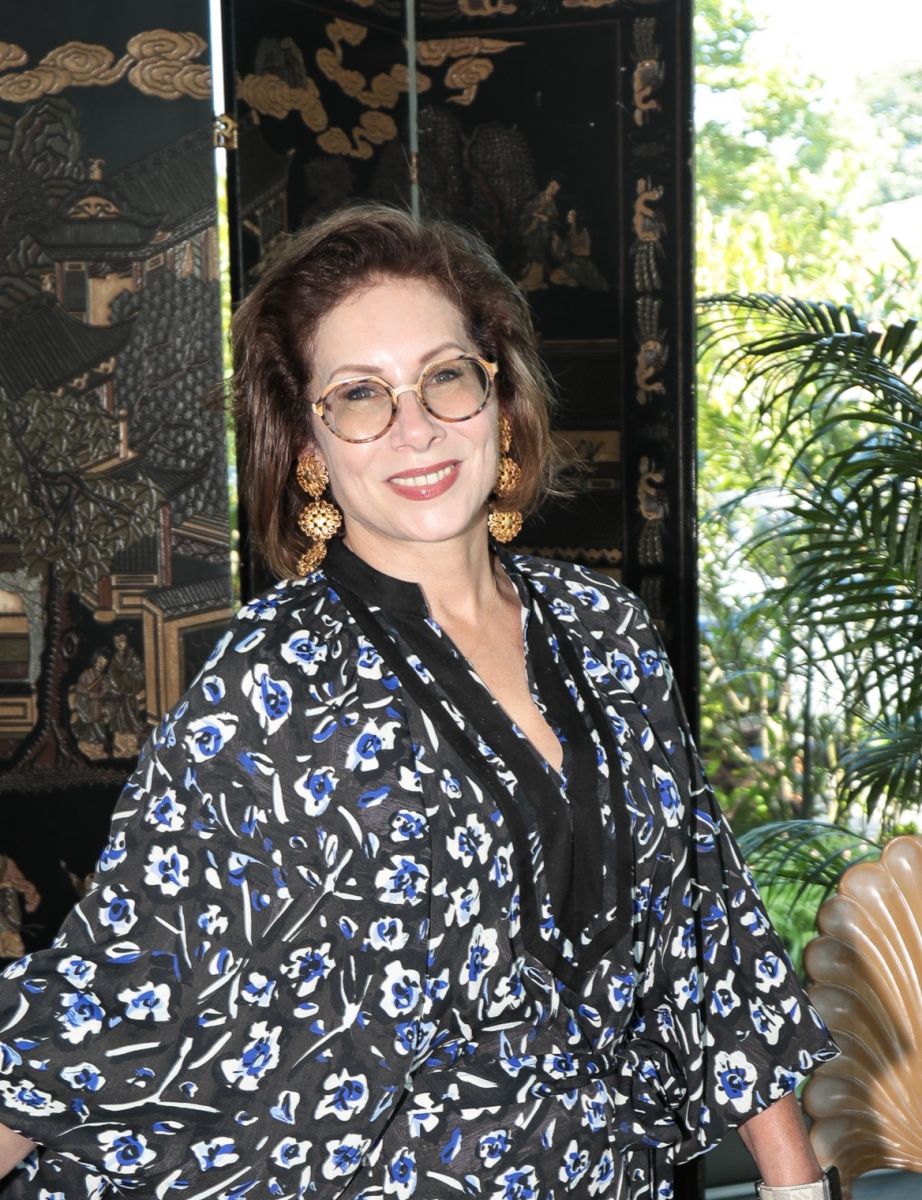 Portrait of interior designer Amal Kapen in front of a large ebonized and gilt Chinese folding screen.