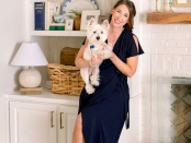 Image of Sally and her puppy smiling in front of a built-in shelf and fireplace, adorned with decorative items such as table lamps, candlesticks, blue and white porcelain pieces, photo frames, and books, against a backdrop of white-painted walls. | BRG
